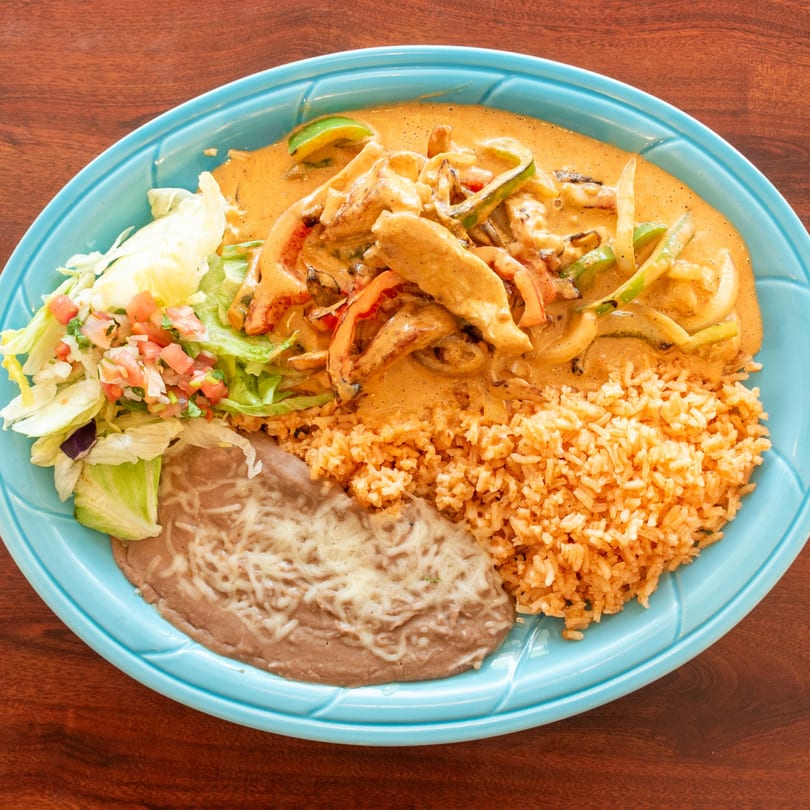 Chicken fajitas in a creamy sauce with rice, refried beans, and a side salad on a blue plate.