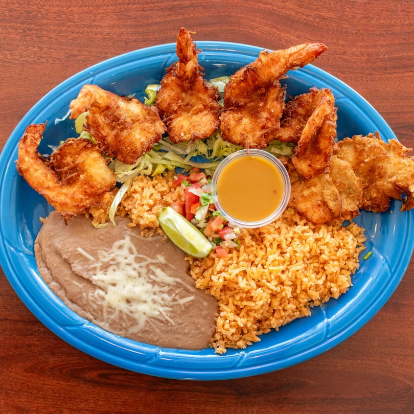 A blue plate with fried shrimp, rice, refried beans, pico de gallo, lime, and dipping sauce.