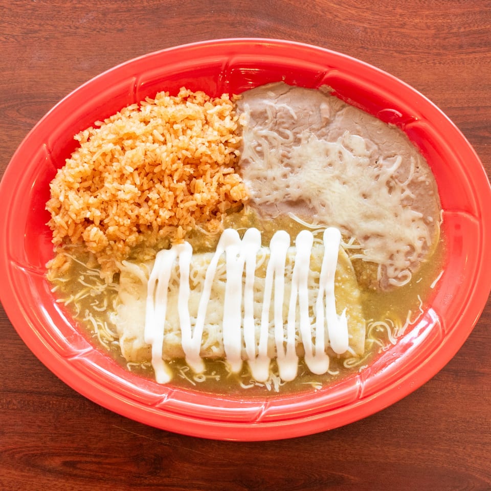 A red plate with enchiladas, rice, and refried beans, drizzled with sour cream.
