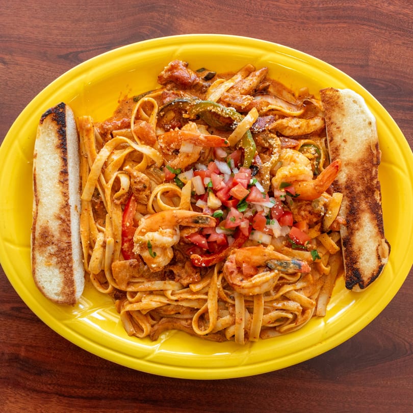 Shrimp fettuccine pasta with red sauce, bell peppers, and pico de gallo, served with toasted bread.