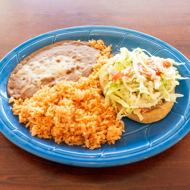 Mexican dish with refried beans, rice, and a sope topped with lettuce, tomato, and crema.
